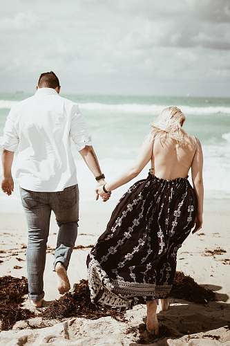 holding hands couple walking on sand near beach during daytime human